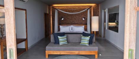 Un dormitorio con cabecera de madera, cama con ropa de cama gris, dos lámparas de noche, una ventana con vistas y una alfombra circular en el suelo.