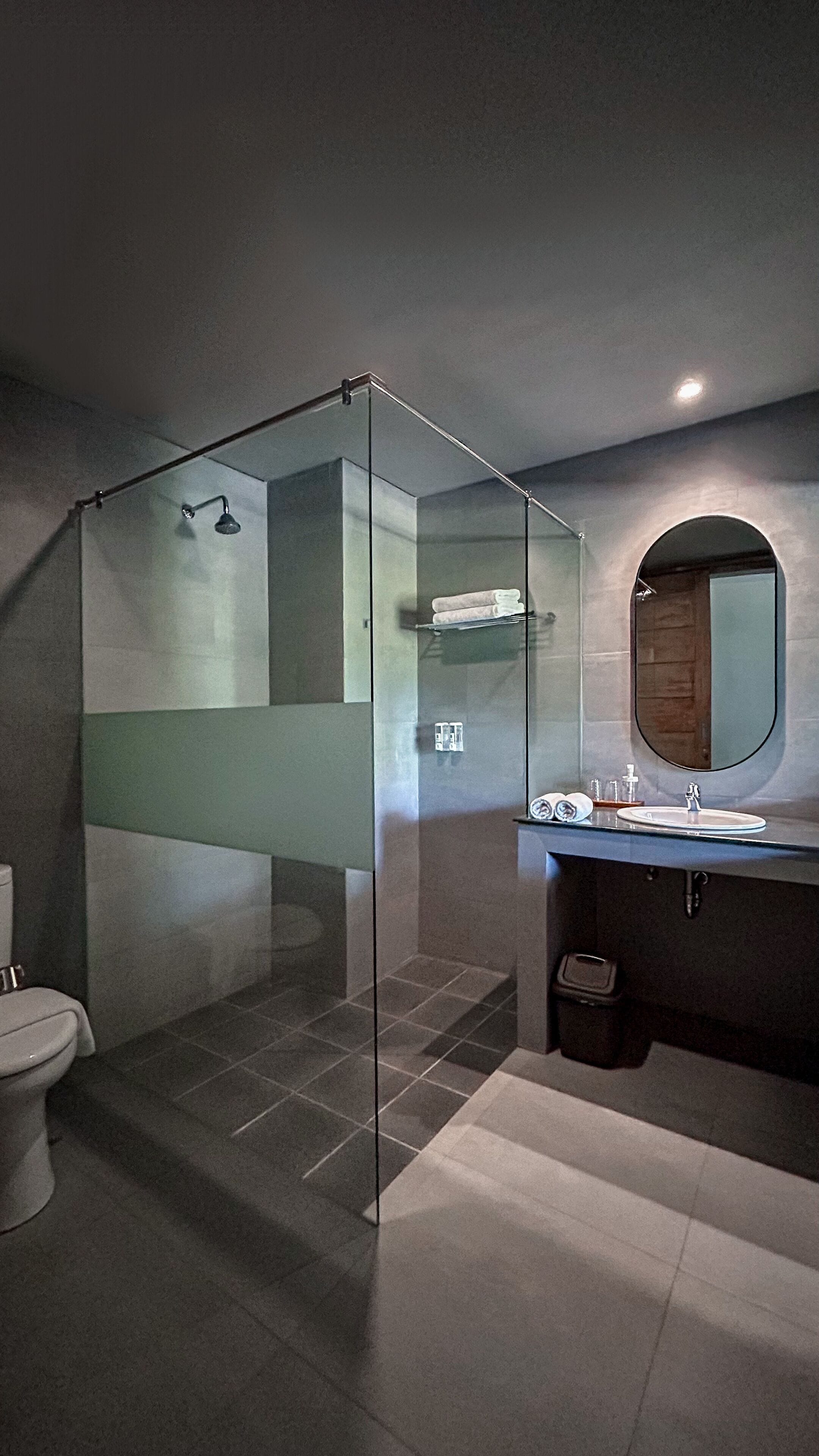 Un baño moderno con ducha de vidrio, espejo redondo y lavamanos integrado.
