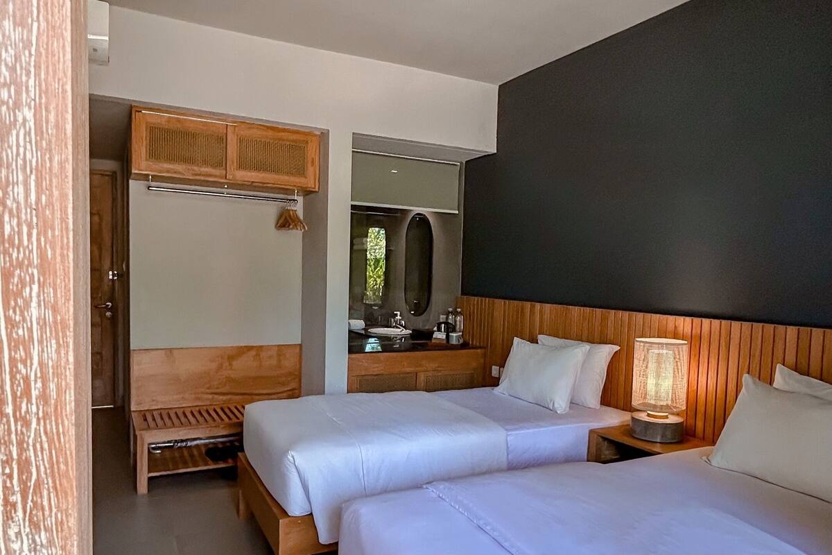 A modern bedroom with two beds, a wooden wardrobe, a vanity with a mirror, and a bedside table with a lamp.