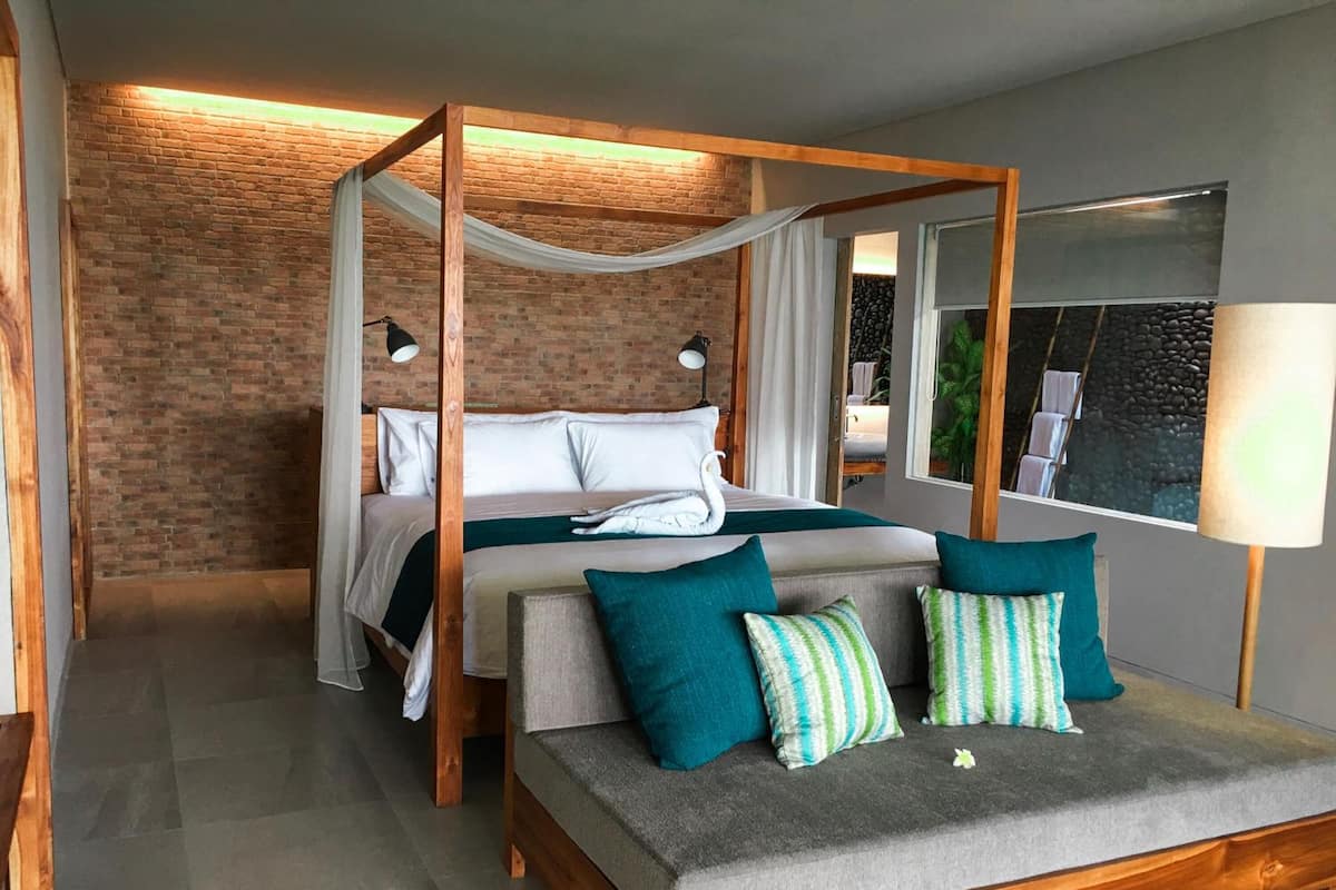 A modern bedroom with a four-poster bed, a sofa, and a large window with a view of a garden.