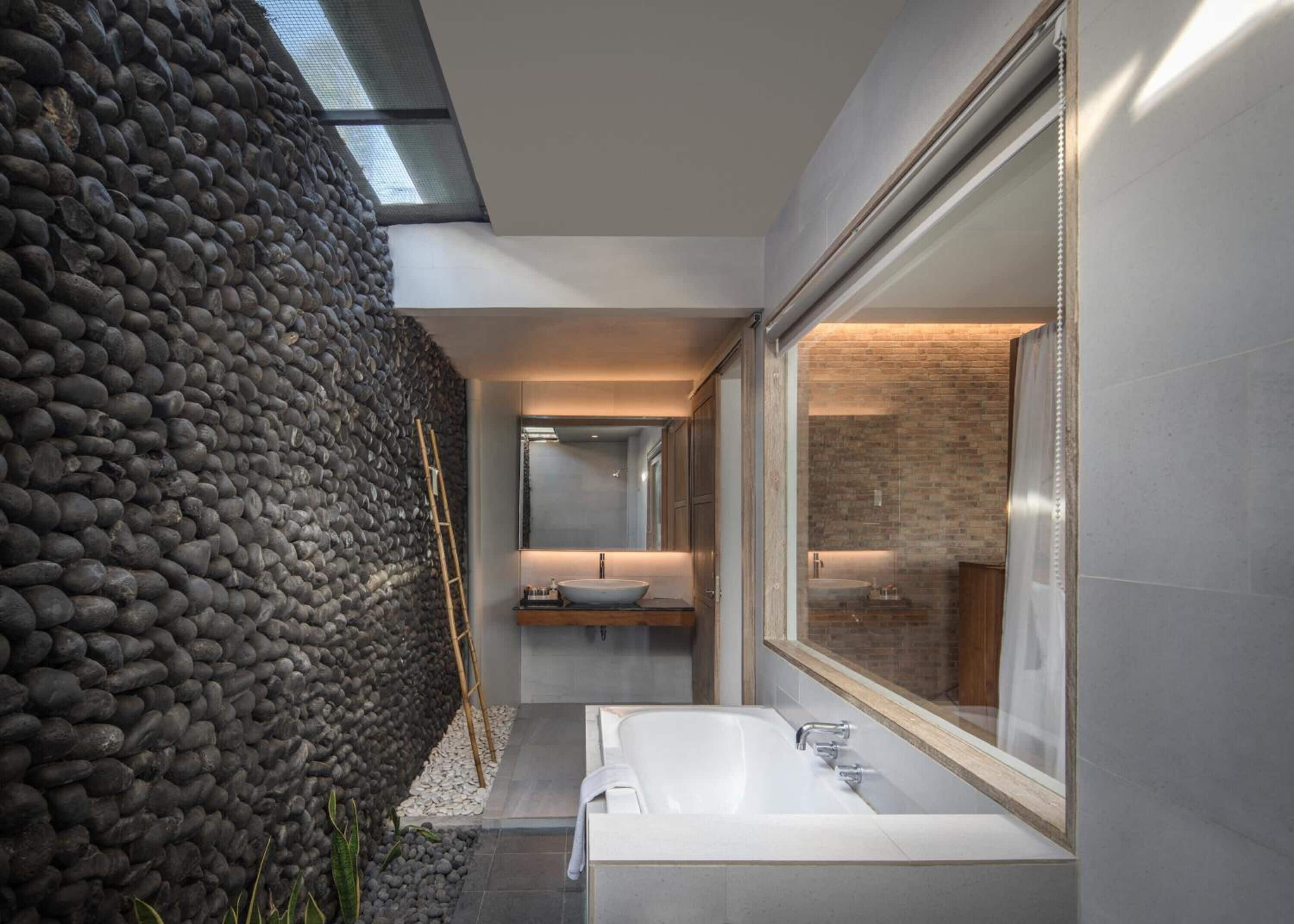 A modern bathroom with a stone wall, a large window, and a bathtub.