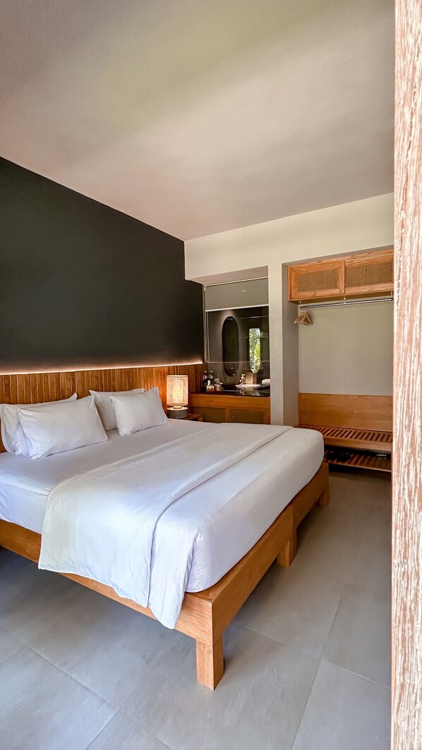 Un dormitorio moderno con una cama grande, cabecera de madera, mesita de noche con lámpara y espejo sobre el lavabo.