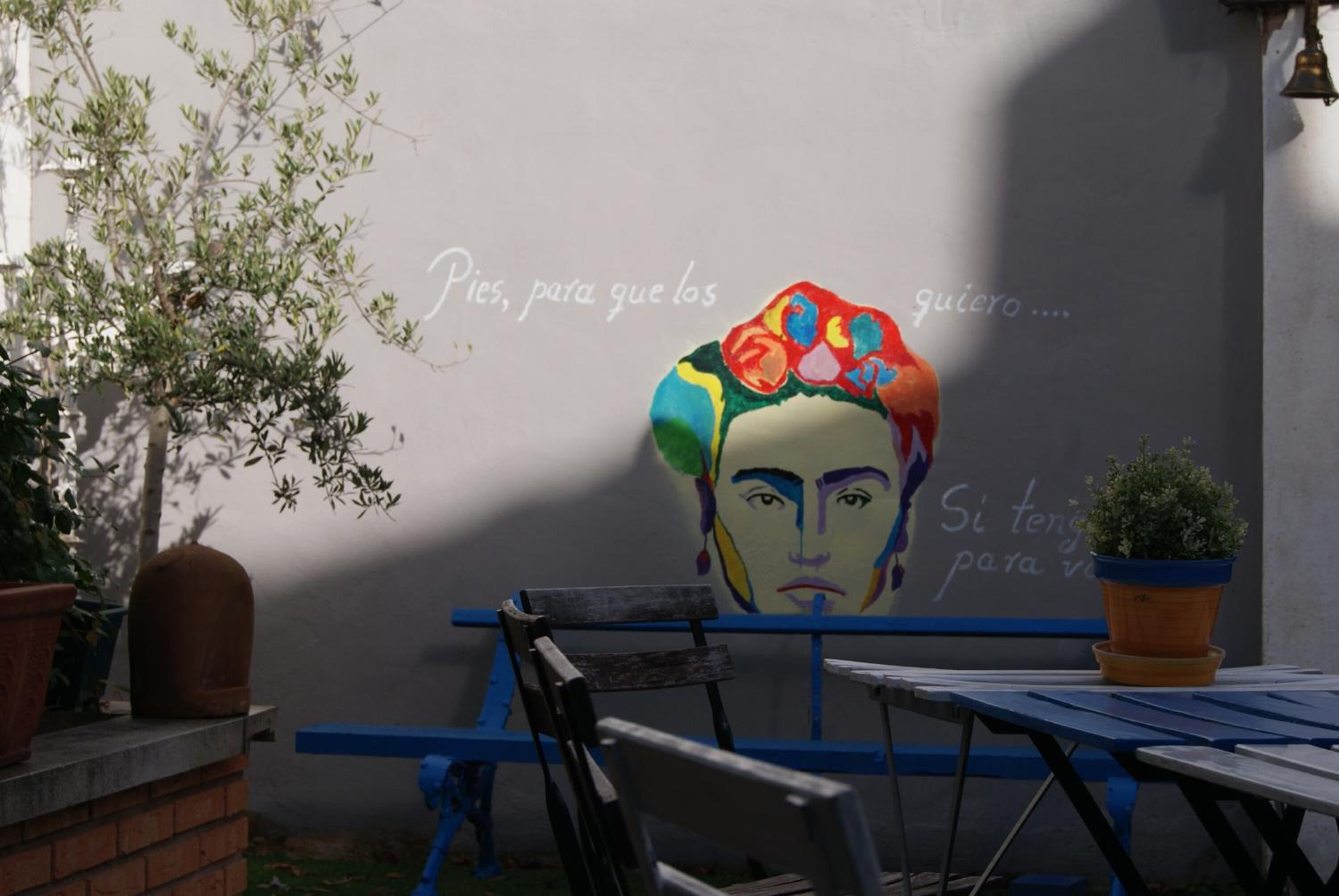 An outdoor seating area with a mural on the wall, a potted plant, and a bench.