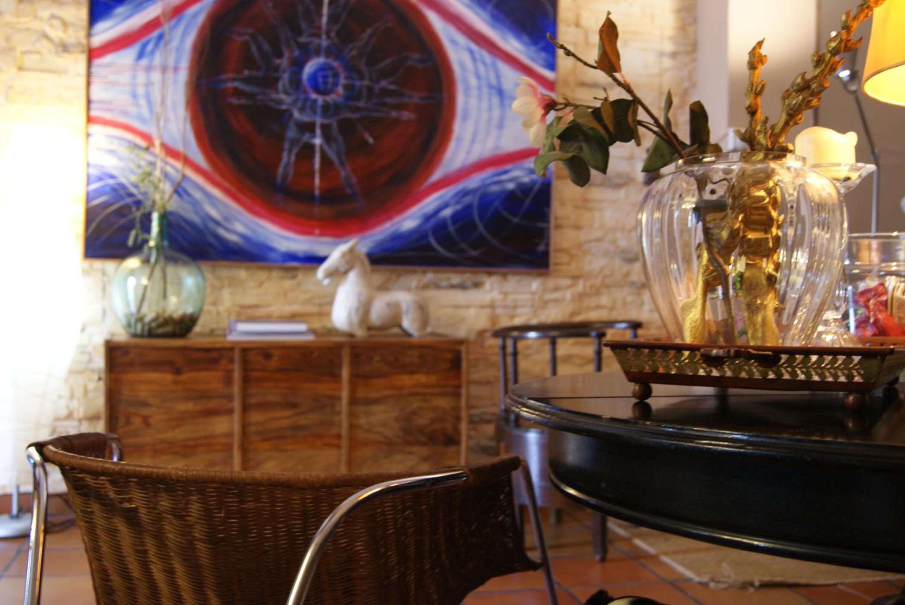 Un comedor con una silla de mimbre, una mesa con un jarrón y un cuadro en la pared.