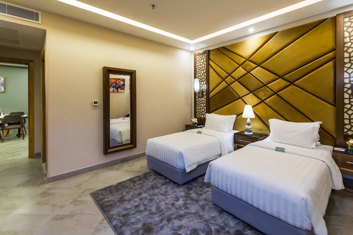 Habitación de hotel con dos camas, una zona de estar con sillas, un espejo y un panel decorativo en la pared.