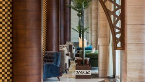 A lobby with a checkered floor, a large wooden column, a decorative screen, and a seating area with a blue sofa. - Boudl Quraish (Jeddah)