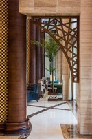 A lobby with a checkered floor, a large wooden column, a decorative screen, and a seating area with a blue sofa.