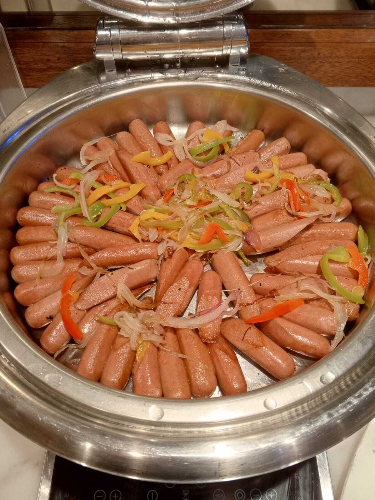 Una plancha de acero inoxidable con salchichas y pimientos en rodajas.