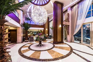 Eine großzügige Lobby mit einem zentralen Kronleuchter, Marmorböden und einer Rezeption.