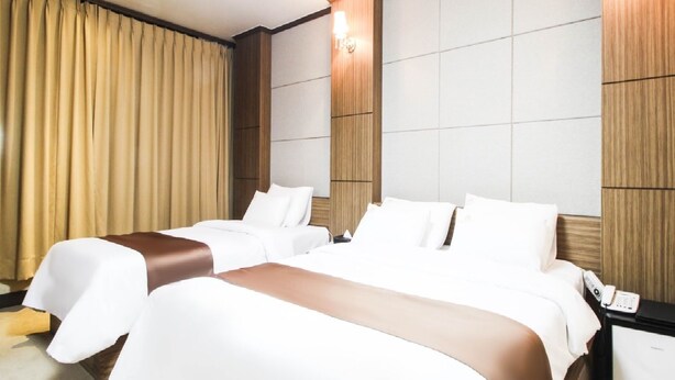 A hotel room with two beds, a nightstand, a lamp, and a large window with curtains. - Uljin Grand Hotel (Uljin)