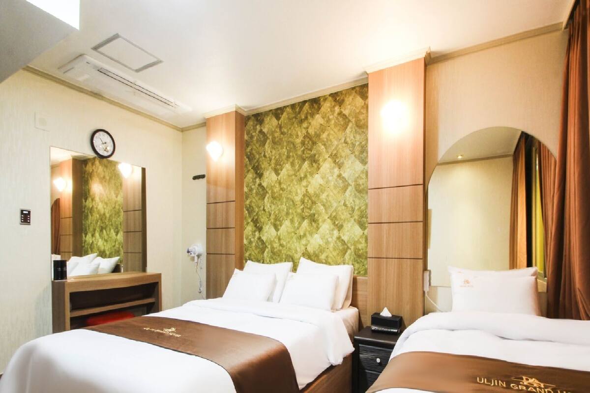 A hotel room with two beds, a large mirror, a clock, and a textured wall.