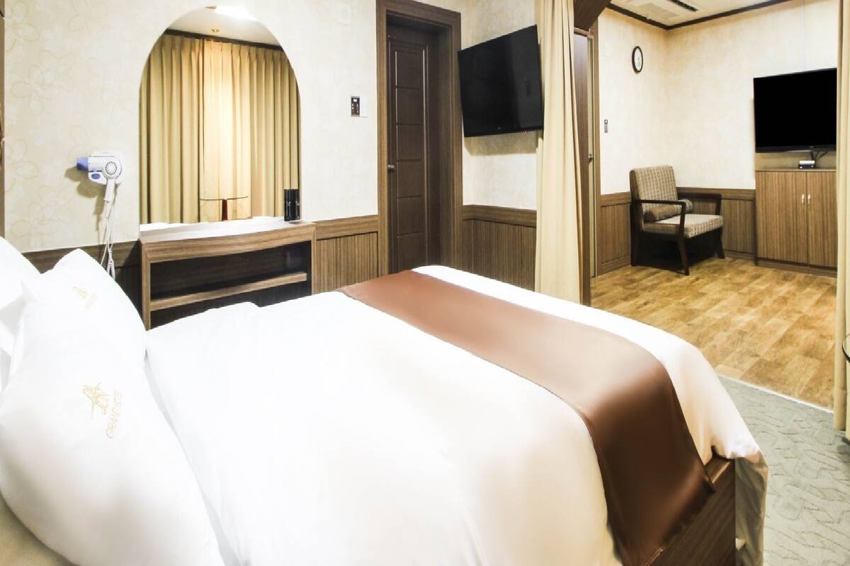 A hotel room with a bed, a TV, a chair, and a desk.