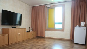 A room with a flat-screen TV, wooden cabinets, a refrigerator, and a window with curtains. - Uljin Grand Hotel (Uljin)