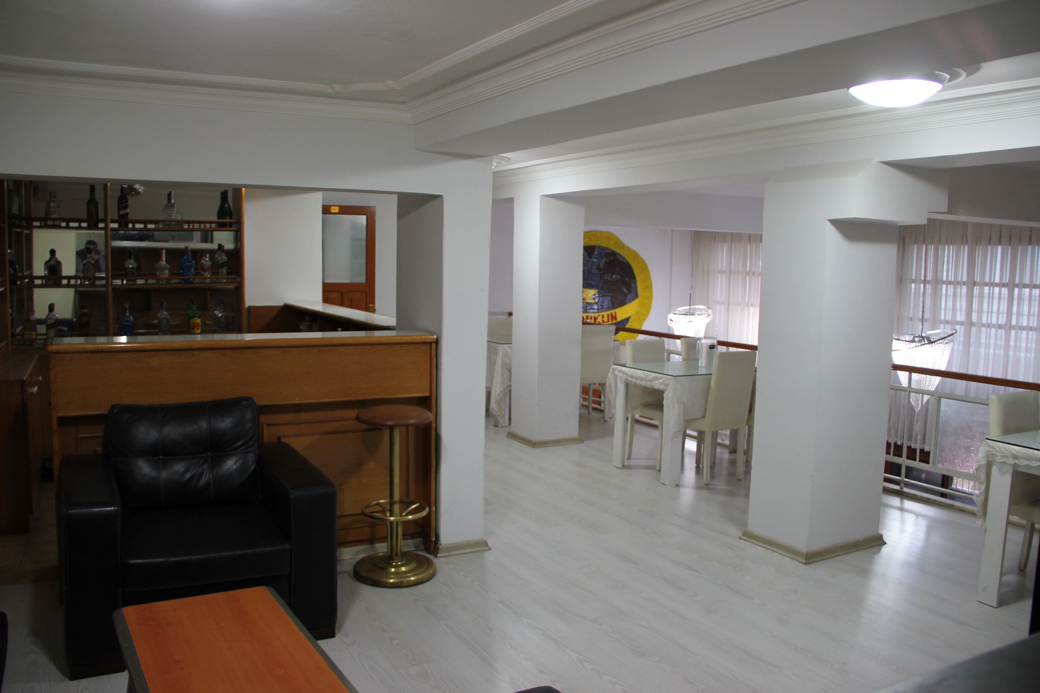 A spacious living area with a black leather sofa, a wooden coffee table, and a bar area with shelves of bottles.