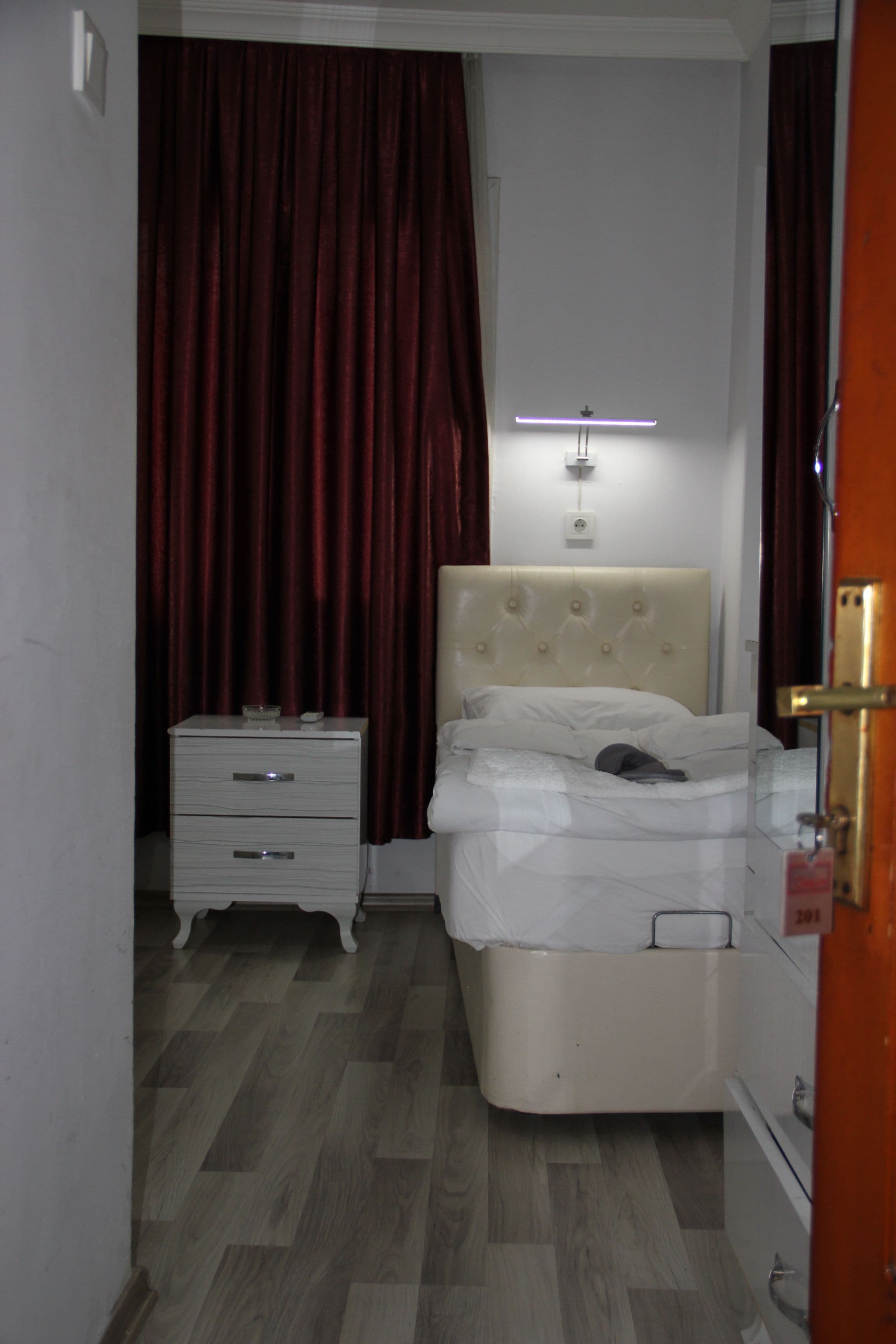 A bedroom with a bed, a nightstand, a bedside table, a lamp, and a door.