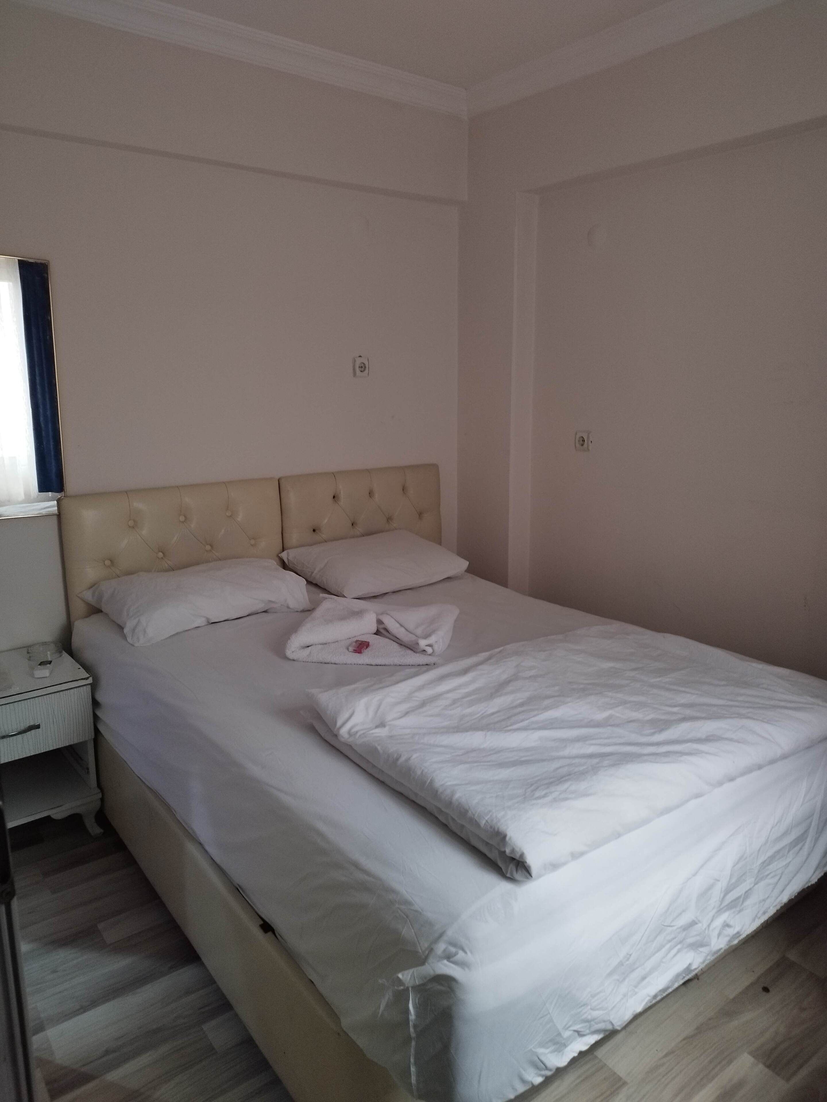 Una cama bien hecha con sábanas blancas y un cabecero, una mesita de noche con una lámpara y un suelo de madera.