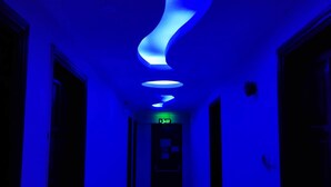 Un pasillo con techo iluminado en azul y una lámpara en el centro.