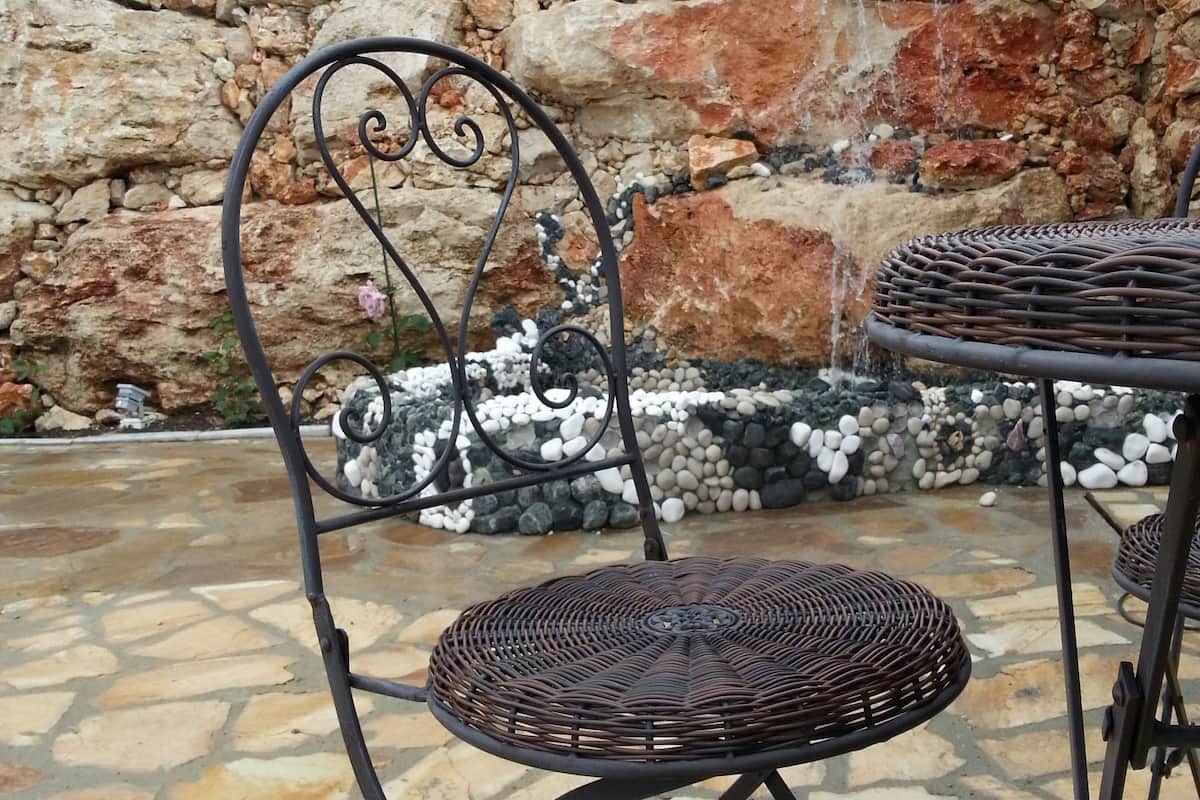 A wicker chair and table set on a stone patio with a stone wall and a view of the sea in the background.