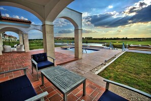 A covered outdoor patio with seating, a pool, and a view of a golf course and residential buildings. - Lighthouse Luxe Estate Apart & Villas (Balchik)