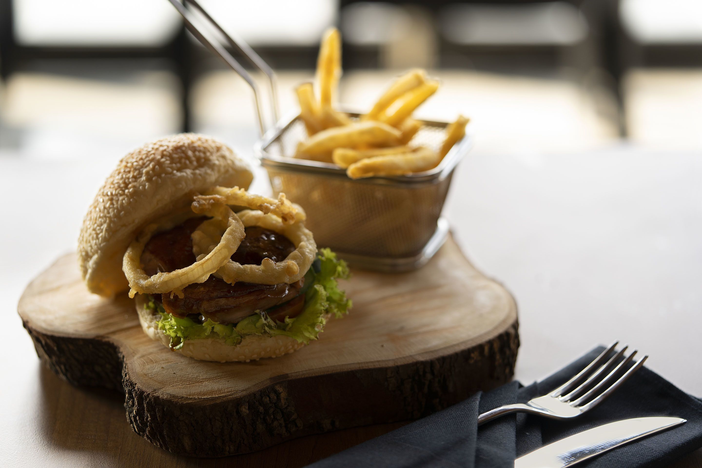 A burger with onion rings and fries on a wooden board.