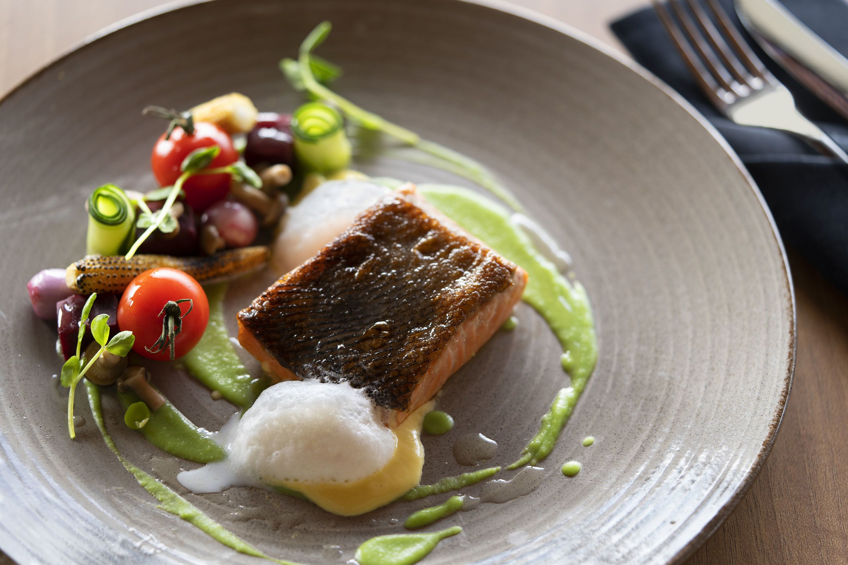A plate with a piece of salmon, cherry tomatoes, and a green sauce.