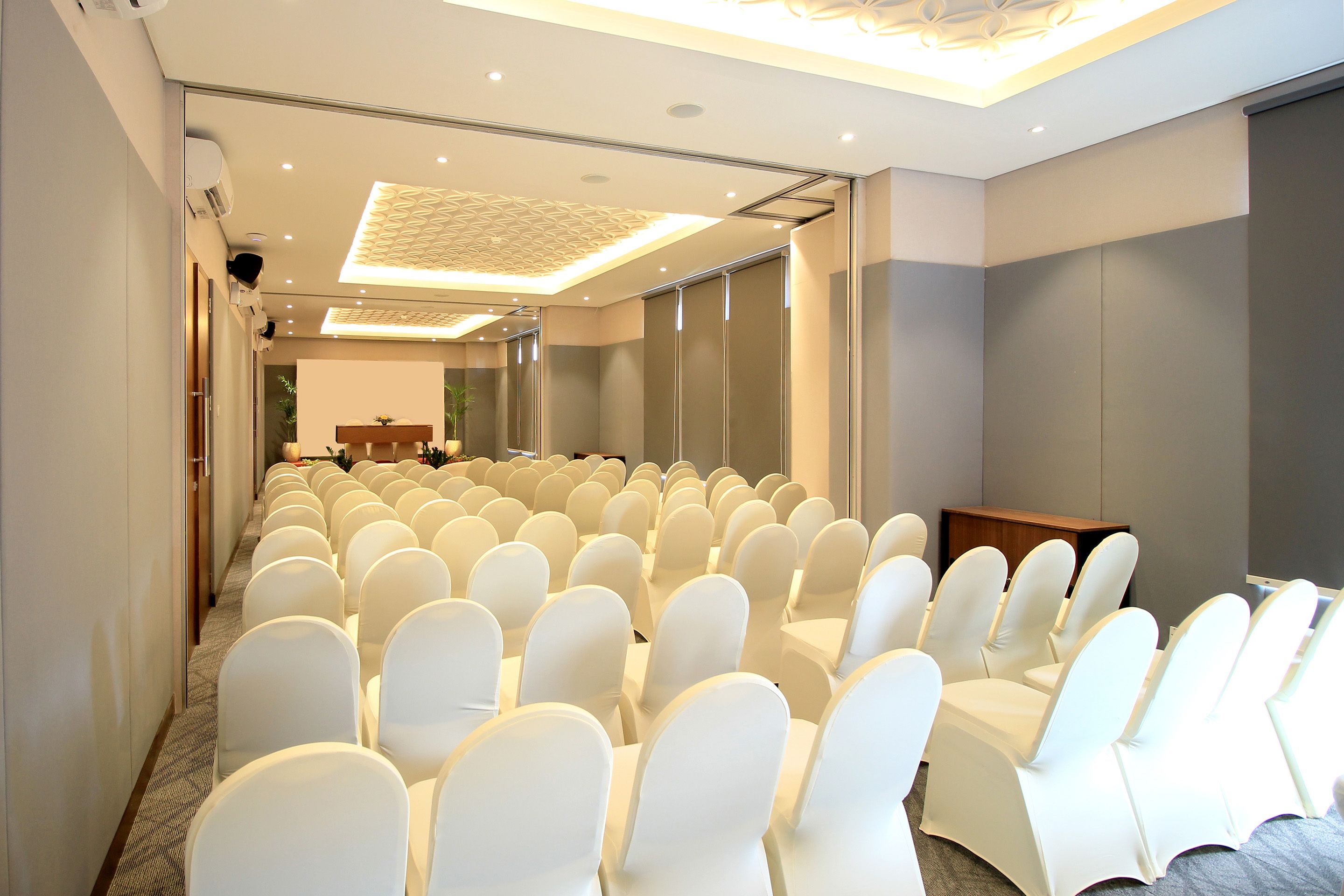 A conference room with rows of white chairs, a wooden podium, and a modern ceiling design.