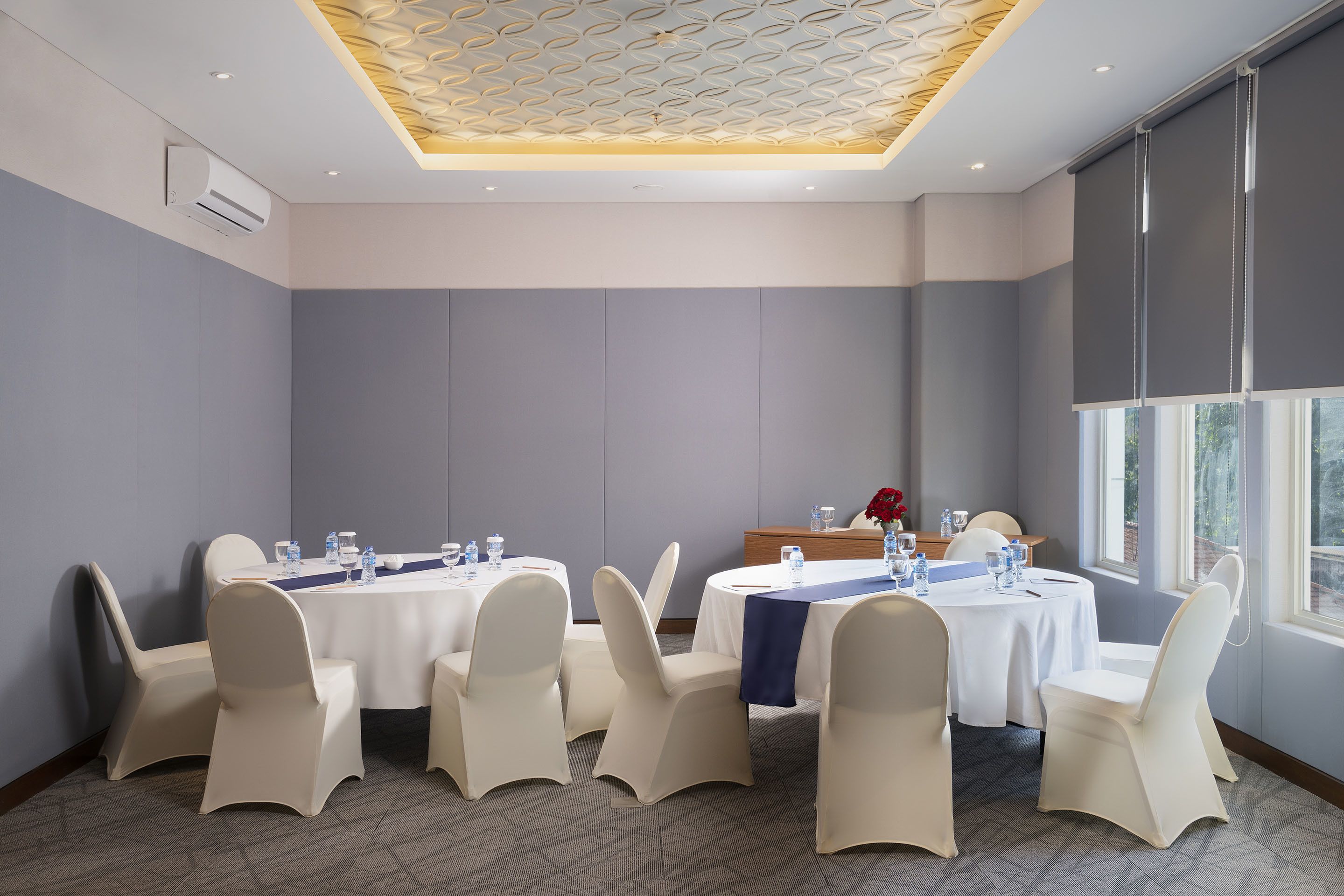 Un salón de conferencias con mesas redondas, sillas blancas y un camino de mesa azul.