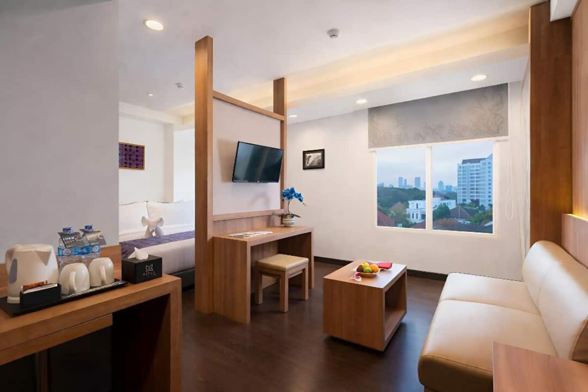 Une chambre d’hôtel moderne dotée d’un bureau en bois, d’un canapé confortable, d’une télévision et d’une grande fenêtre donnant sur la ville.