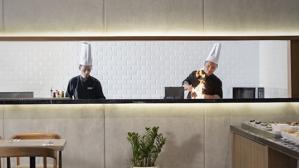 A modern kitchen with two chefs, a brick wall, and a buffet area.