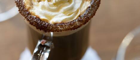 A close-up of a beverage with whipped cream and a cinnamon stick, served in a glass mug.