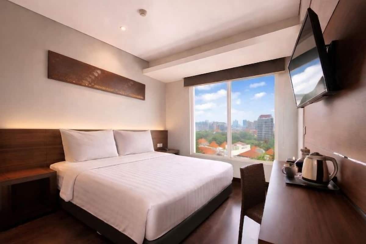 Une chambre d’hôtel avec un lit, une télévision, un bureau avec une bouilloire et une vue sur la ville.