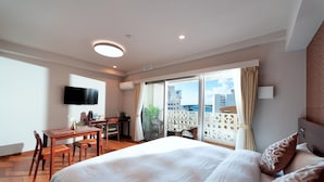 A hotel room with a bed, a desk, a chair, a TV, and a balcony with a view of the city.