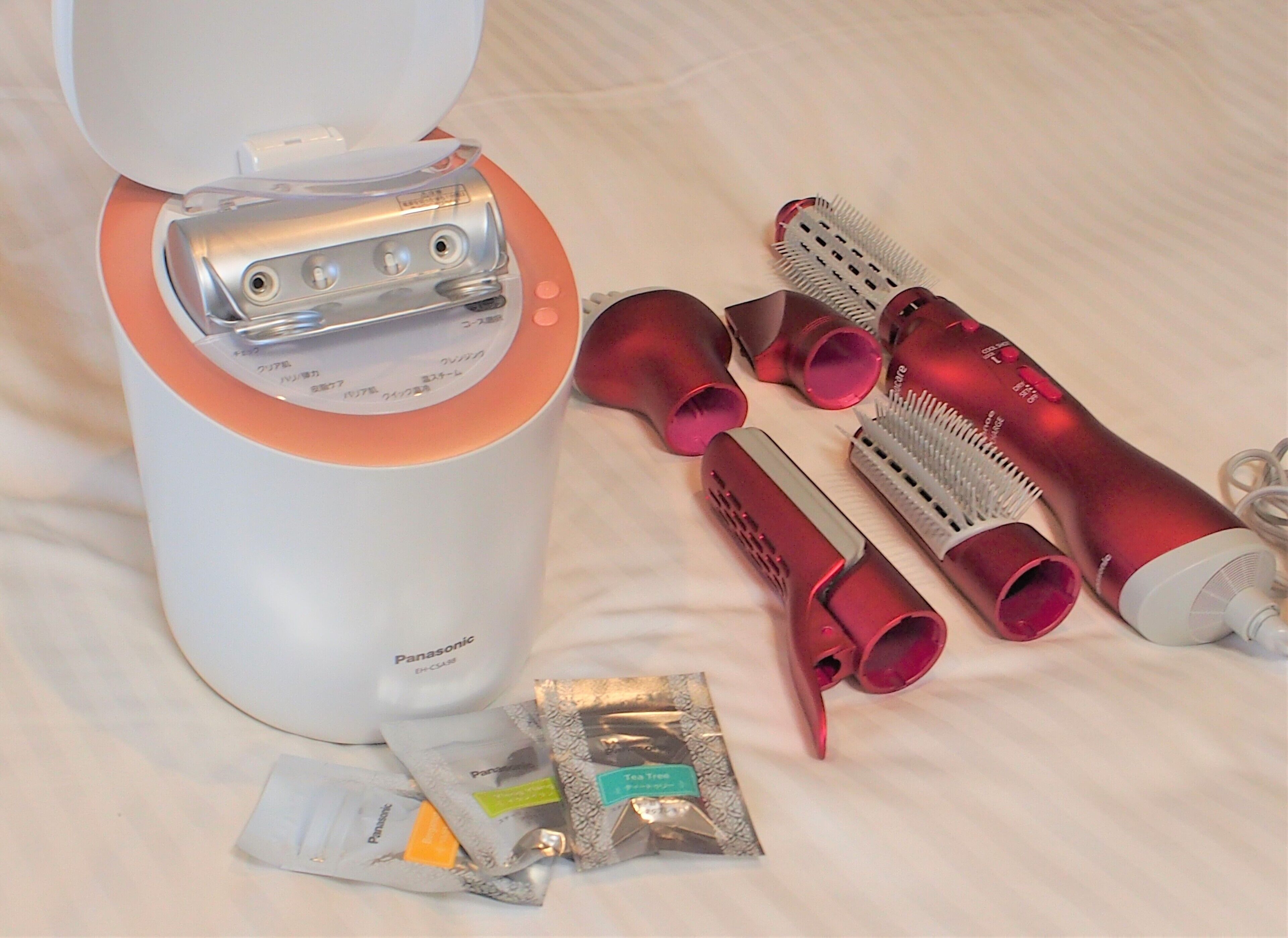 A Panasonic hairdryer, several hairbrushes, and a few packets of hair care products on a bed.
