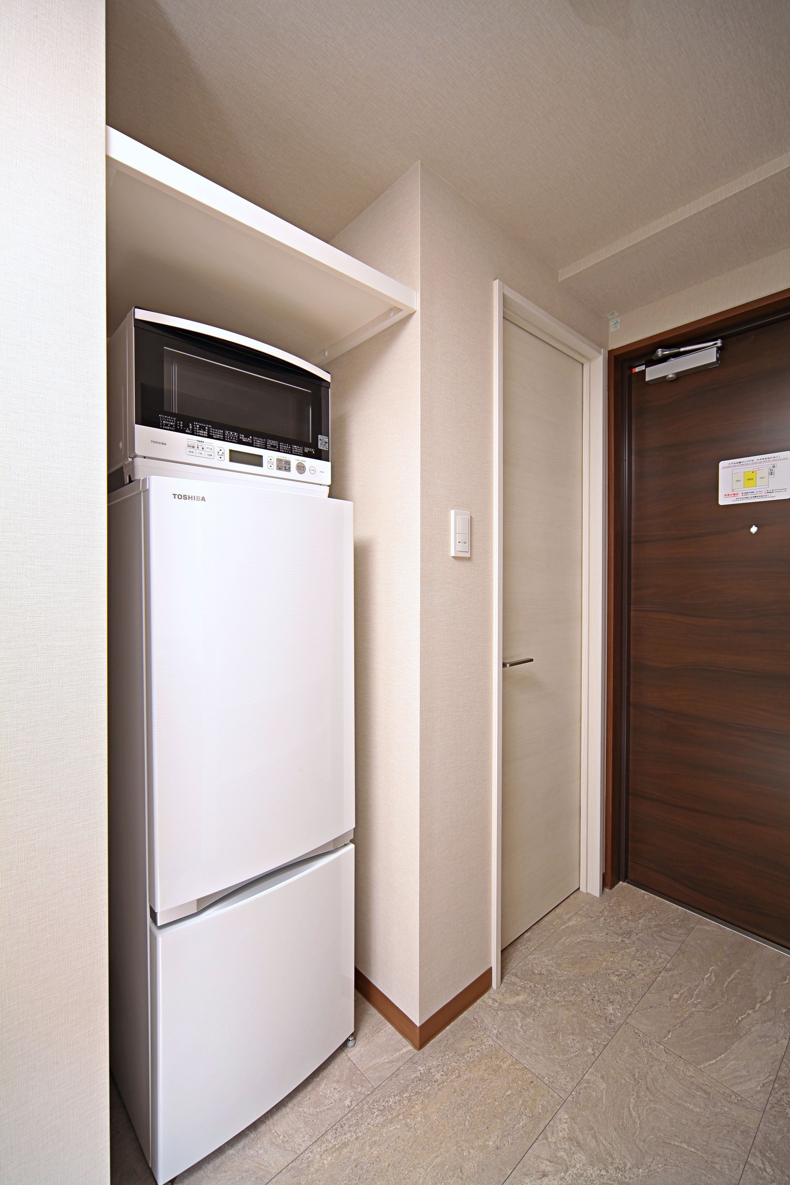 A compact kitchen with a white refrigerator, a microwave, and a wooden door.