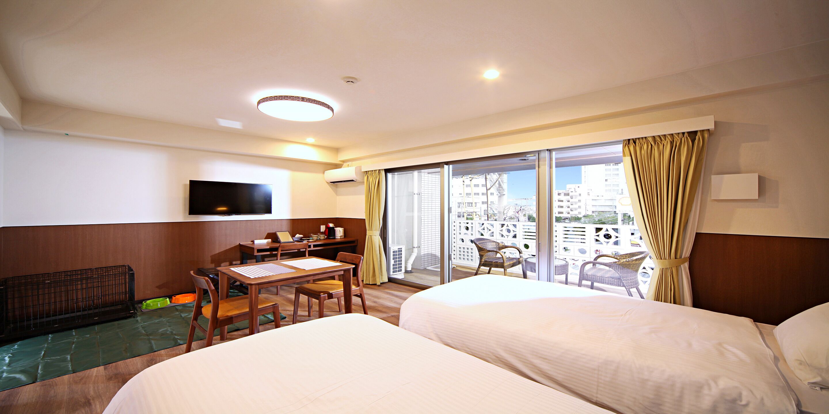 Une chambre d’hôtel avec deux lits, un bureau avec une chaise, un téléviseur fixé au mur et un balcon offrant une vue sur la ville.