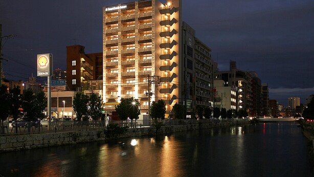 A multi-story hotel with a Shell sign, located beside a river. - SmartCondo Tomari (Naha)