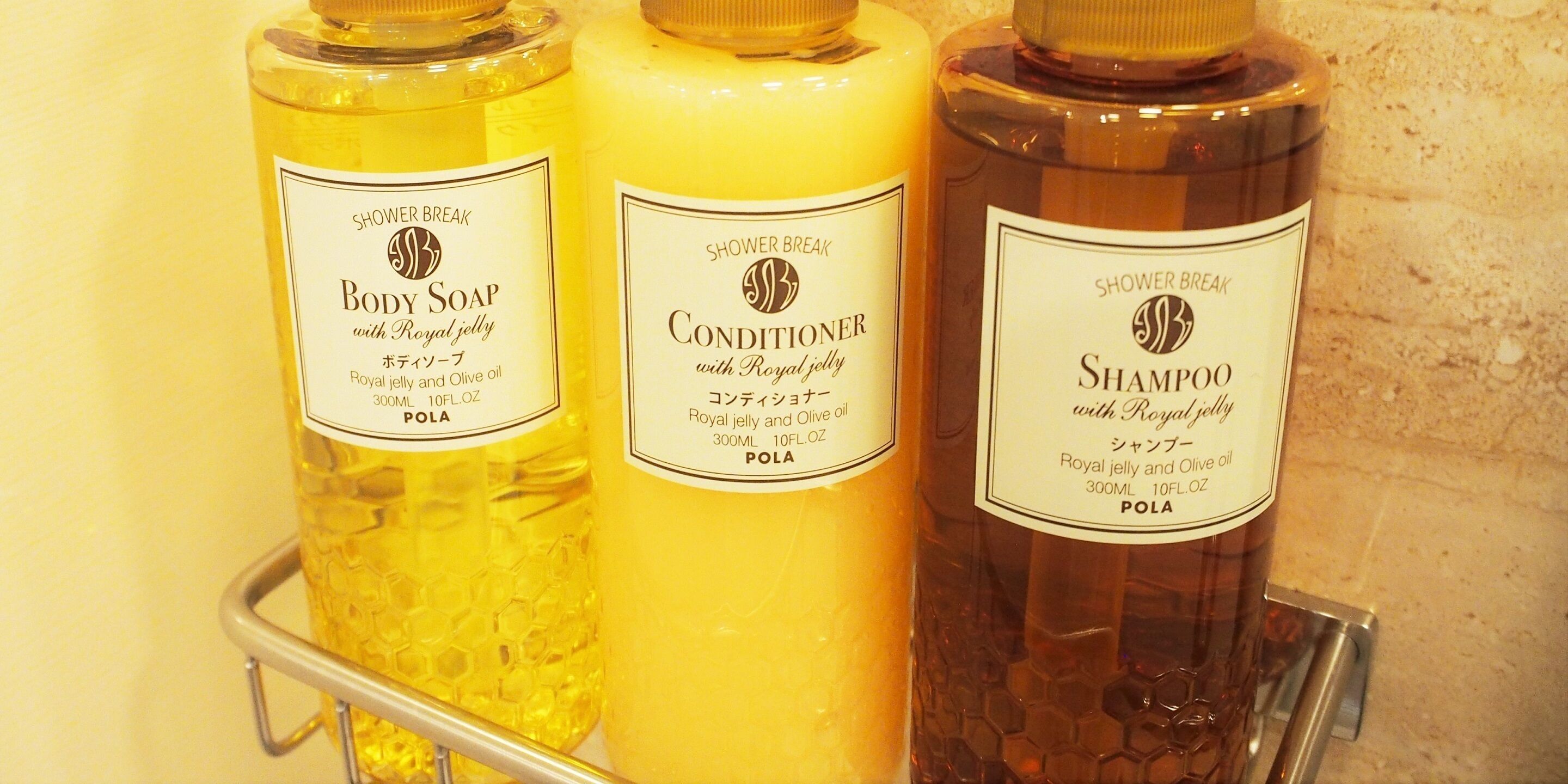 Tres botellas de productos Shower Break para el cuidado corporal en un estante metálico.