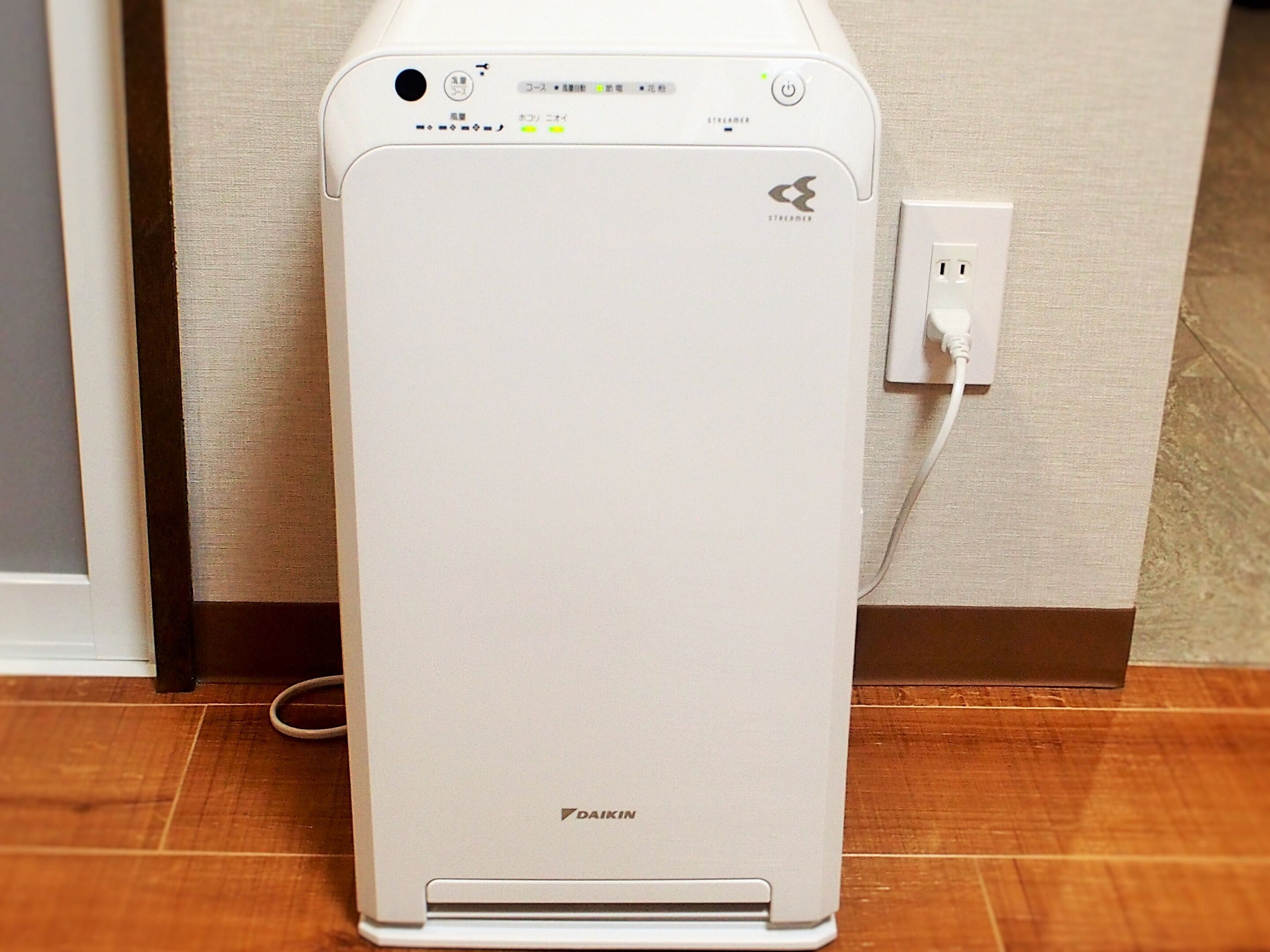 A white Daikin air conditioner unit with a power cord plugged into a wall socket.