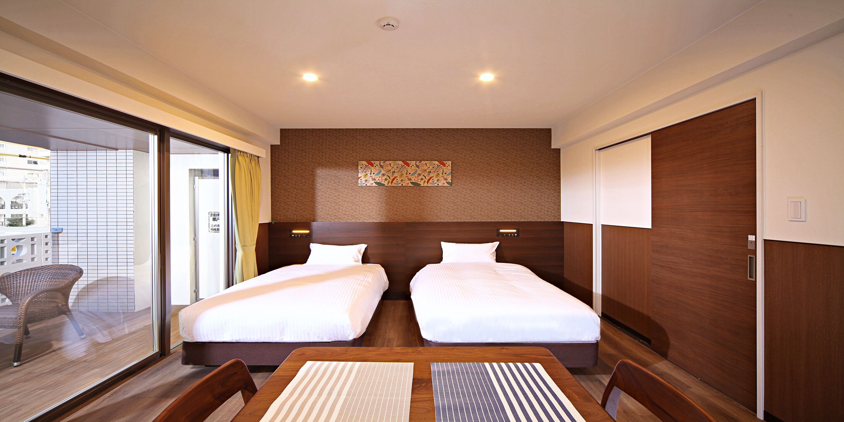 Habitación de hotel con dos camas, una mesa de comedor y vistas al balcón exterior.