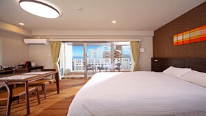 A hotel room with a large bed, a desk, and a chair. There is a balcony with a view of the city. - SmartCondo Tomari (Naha)