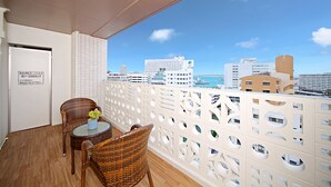 A balcony with wicker chairs and a small table, overlooking a cityscape with buildings and a body of water.