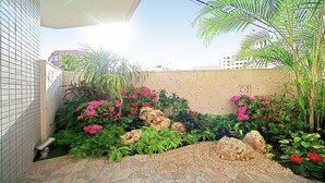 A garden with various plants, rocks, and a tiled wall. - SmartCondo Tomari (Naha)