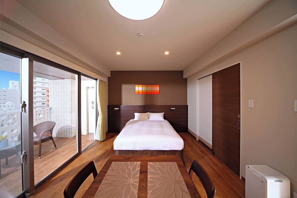 Ein modernes Hotelzimmer mit einem großen Bett, einer Schiebetür zu einem Balkon und Blick auf die Skyline der Stadt.