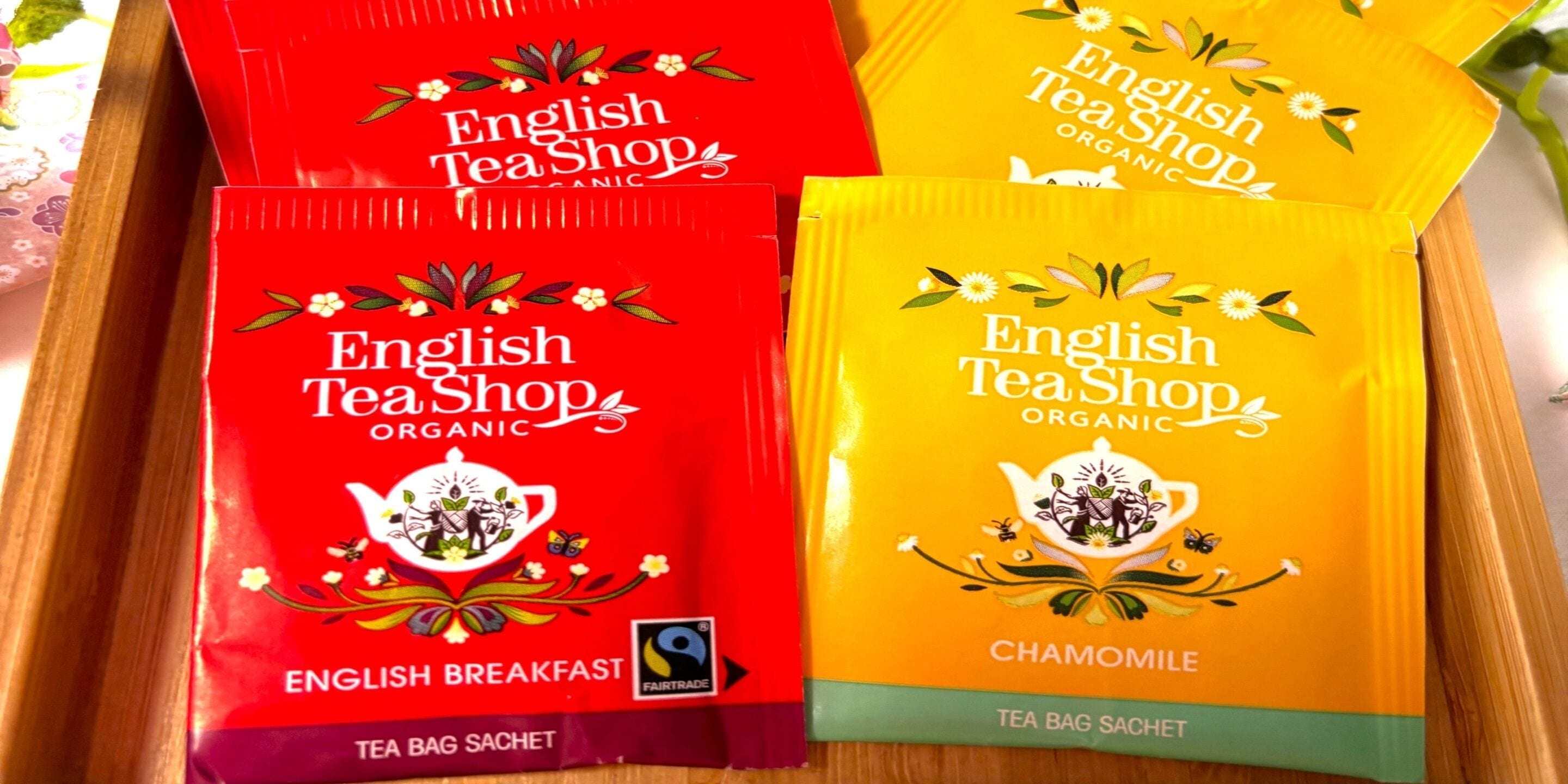Cuatro bolsitas de té de English Tea Shop, dos rojas y dos amarillas, con etiquetas que indican 'English Breakfast' y 'Manzanilla'.