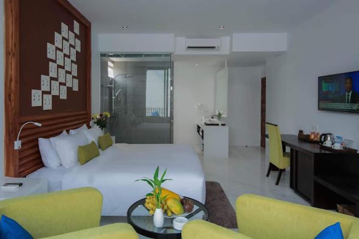 A modern hotel room with a large bed, a desk, a television, and a seating area with yellow chairs.