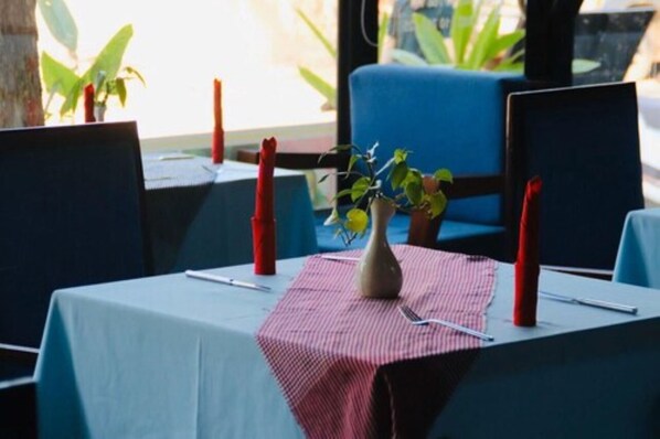 A dining table with a vase of flowers, red candles, and a checkered tablecloth.