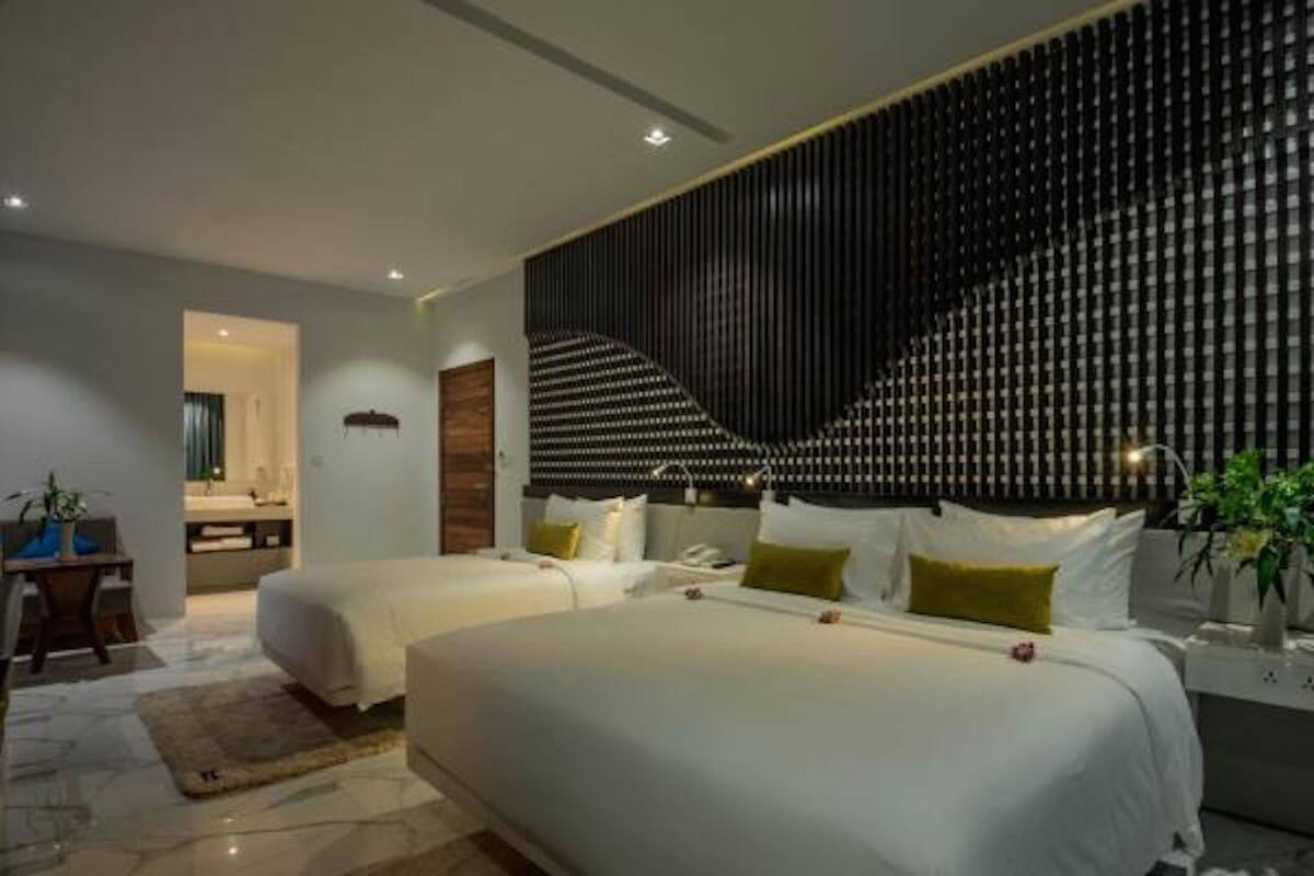 A modern hotel room with two beds, a large wall panel, and a small desk with a chair.