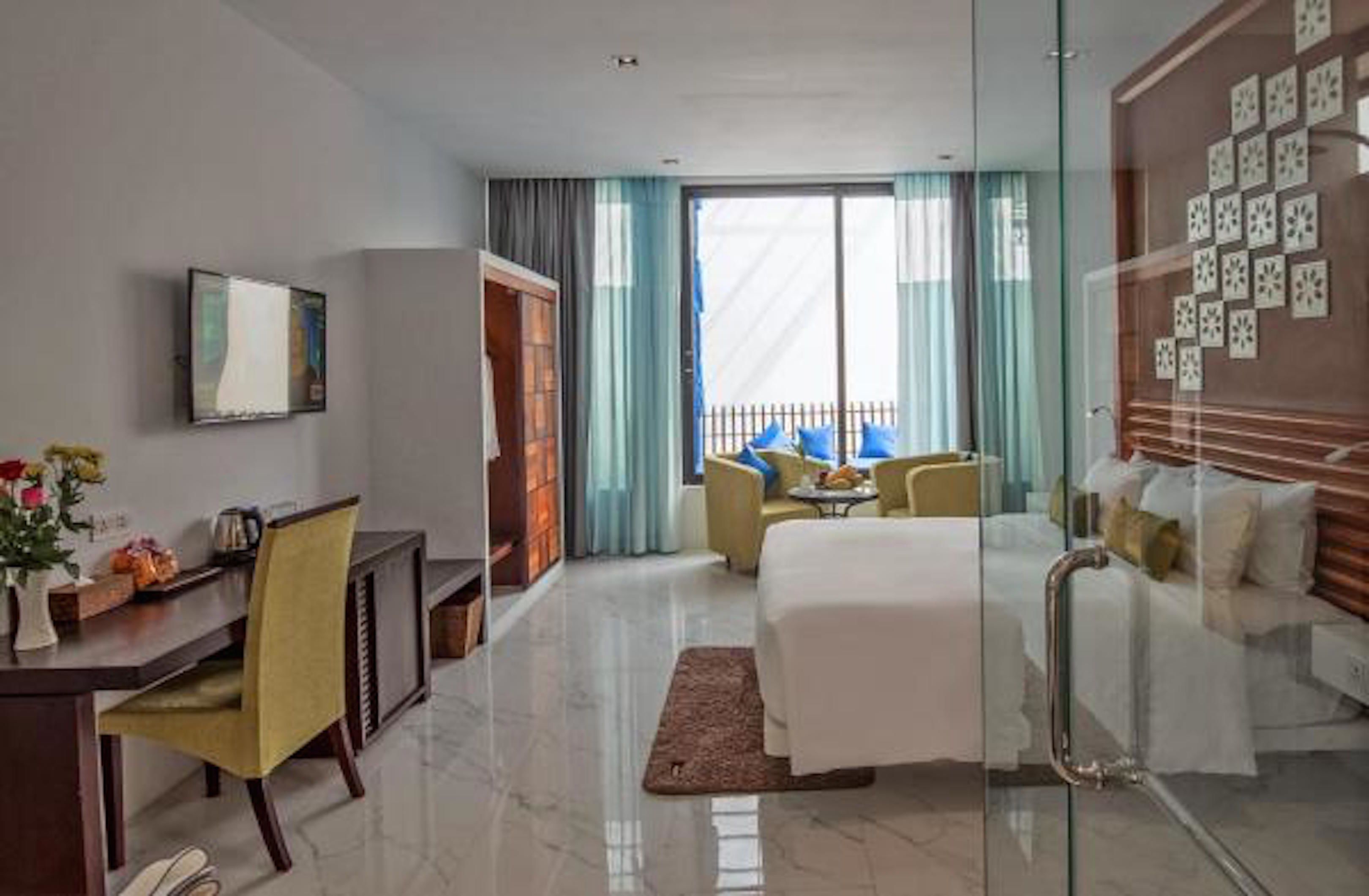 Ein Hotelzimmer mit Bett, Schreibtisch, Stuhl, Sofa und einem Balkon mit blauen Vorhängen.