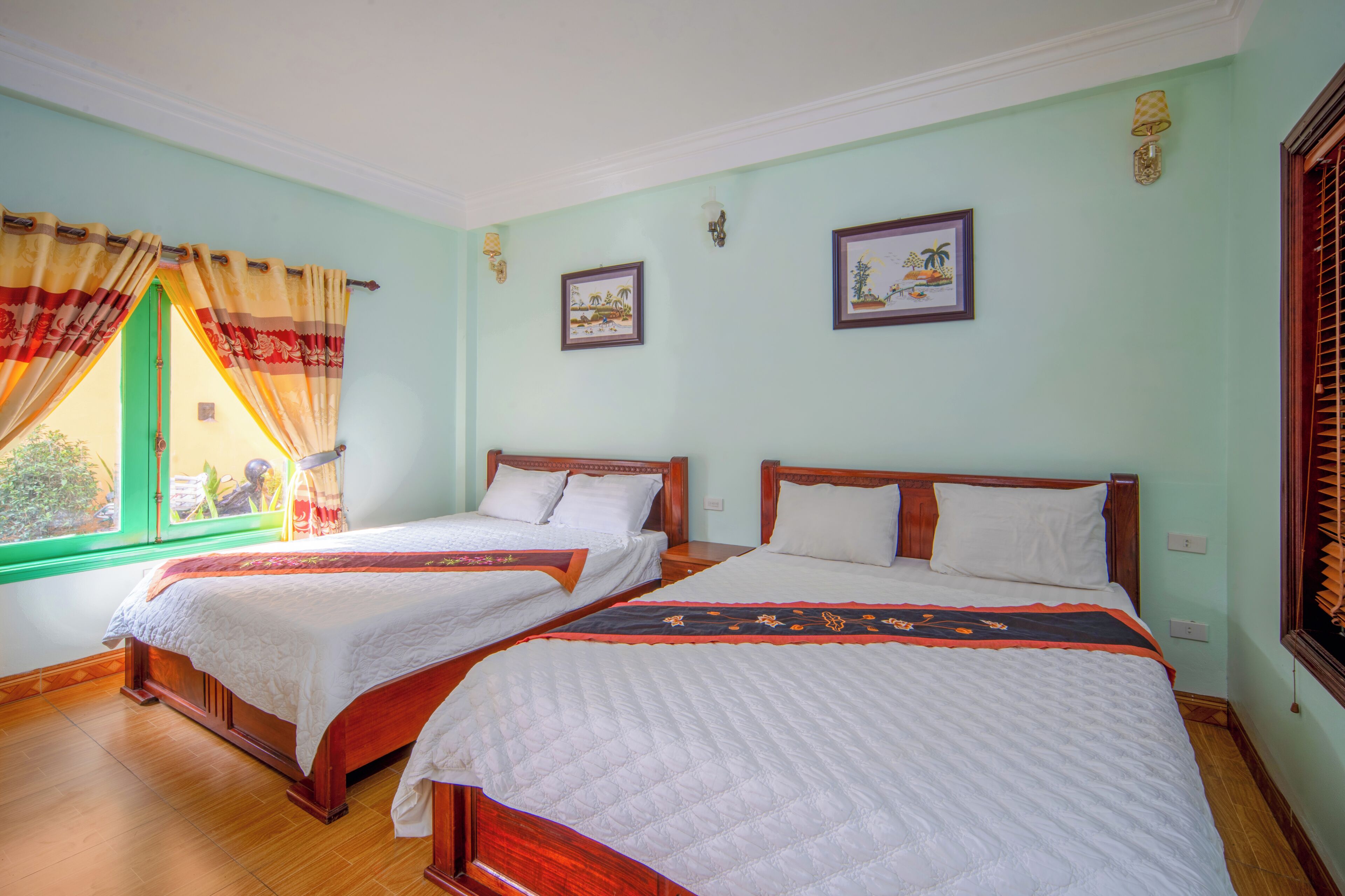 Une chambre avec deux lits, une fenêtre avec des rideaux et deux tableaux accrochés au mur.