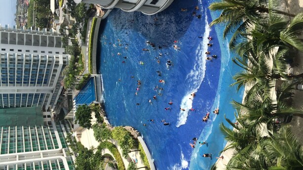 A large indoor swimming pool with multiple lanes, surrounded by palm trees and modern buildings. - Family Condo by IA at Azure Urban Resort Residences (Parañaque)